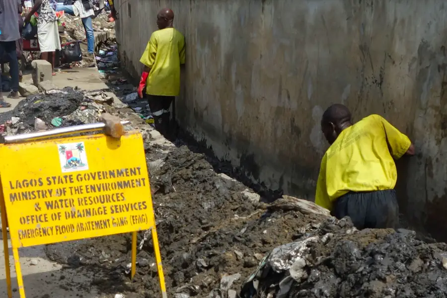 Lagos State drainage services crews clearing silt from a street drain beside a Ministry of the Environment sign