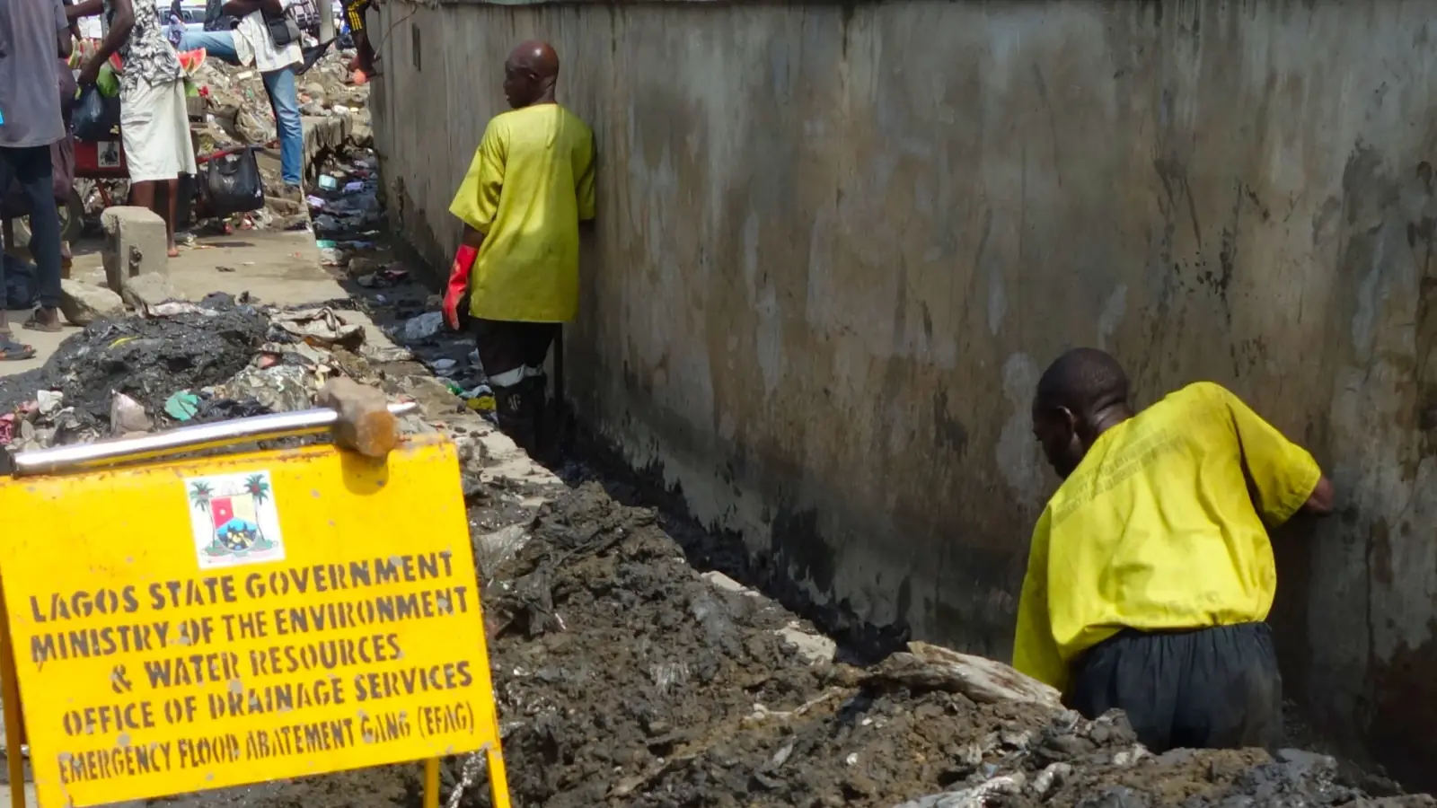 Lagos State drainage services crews clearing silt from a street drain beside a Ministry of the Environment sign
